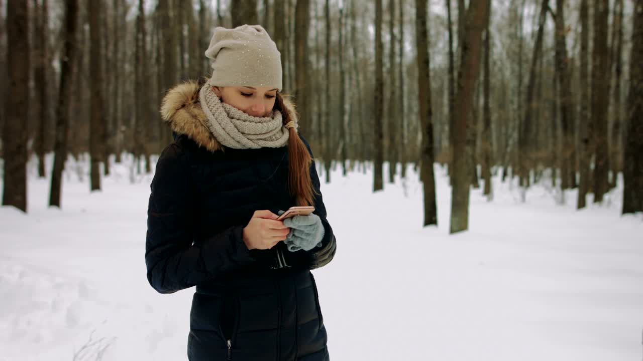 hermosa joven sonriente usando el móvil en el parque de invierno