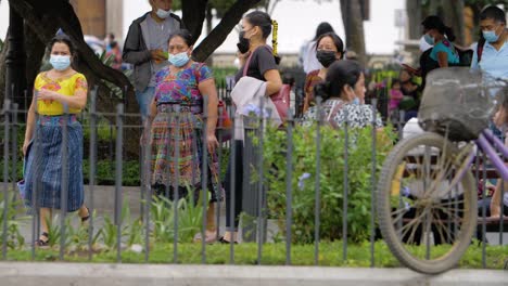 antigua guatemala three native indigenous women with traditional dresses walk along a busy town square wearing face masks due to pandemic along with various pedestrians - handheld slow motion