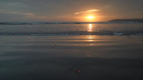 seascape view of ocean waves crashing on the sandy shoreline, at sunset, on a cloudy evening