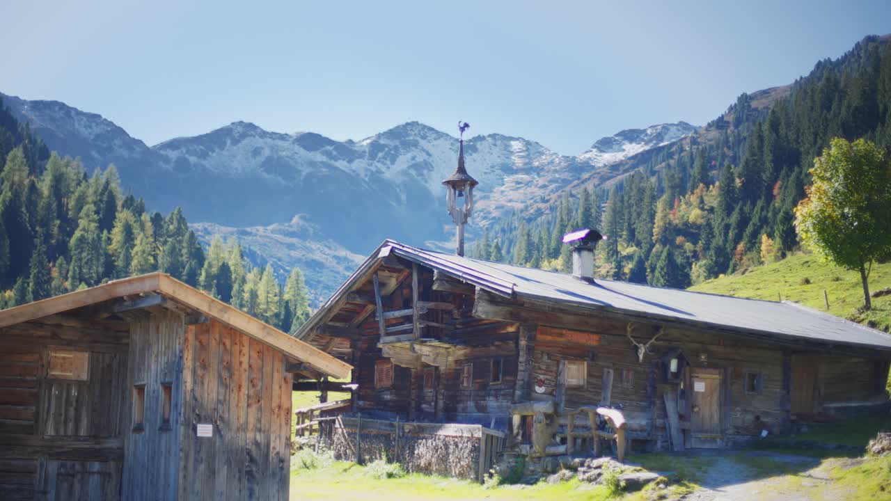 antigua cabaña alpina de madera con un paisaje alpino con pastos verdes, árboles y montañas al fondo en un claro día de verano