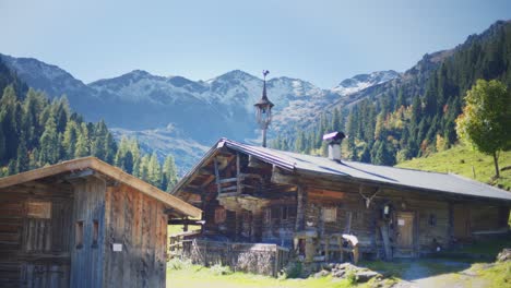 Old-wooden-alpine-hut-with-an-alpine-landscape-with-green-pastures,-trees-and-mountains-in-the-background-on-a-clear-summer-day