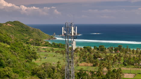 La-Torre-De-Telefonía-Celular-Tiene-Vistas-A-Los-Exuberantes-Campos-De-Arroz-Y-A-Pantai-Lancing,-Lombok,-Con-El-Océano-Y-Las-Colinas-De-Fondo.