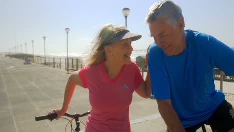 vista frontal de una pareja caucásica senior activa interactuando entre sí en un paseo marítimo en la playa 4k