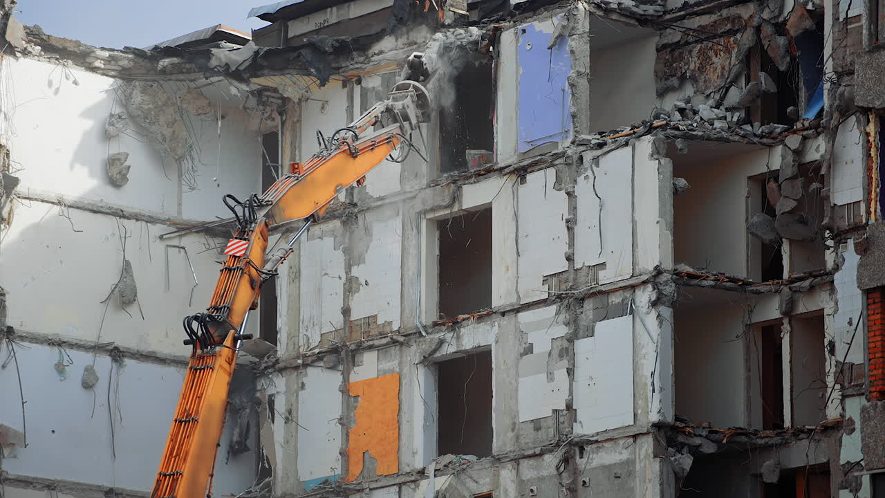 Dismantling the destroyed roof of a high building. Excavator grabber reaches high to demolish the house.