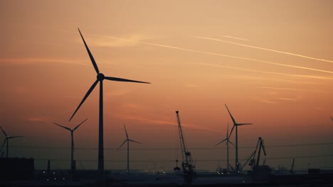 wind turbines spin beneath a sunset sky streaked with airplane contrails, contrasting clean energy with the surrounding industrial setting and heavy air traffic