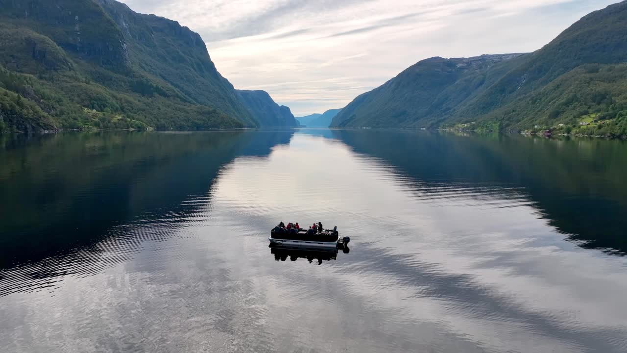 Drone orbits and descends around a pontoon boat in Veafjord, revealing the endless fjord in the back