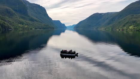 drone orbits and descends around a pontoon boat in veafjord, revealing the endless fjord in the back
