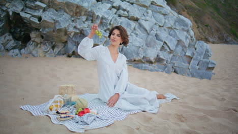 mujer haciendo picnic en la playa en el acantilado del océano. dama sonriente sosteniendo frutas sabrosas