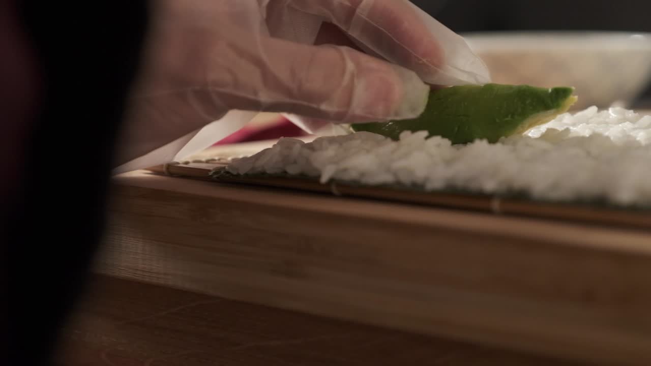 Kuchař připravuje sushi rolky v kuchyni.