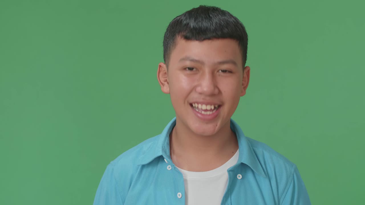 Smiling Young Asian Boy Positively Shaking His Head At The Camera In The Green Screen Studio