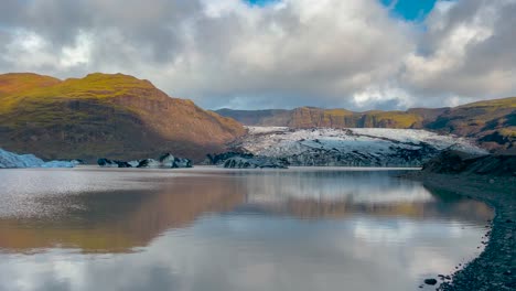 el sol ilumina el glaciar sólheimajökull en islandia que se refleja en un lago sereno, con un cielo dramático