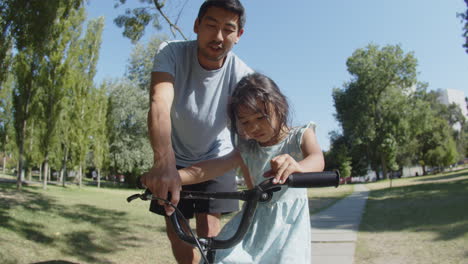 little asian girl riding bike with her father in park