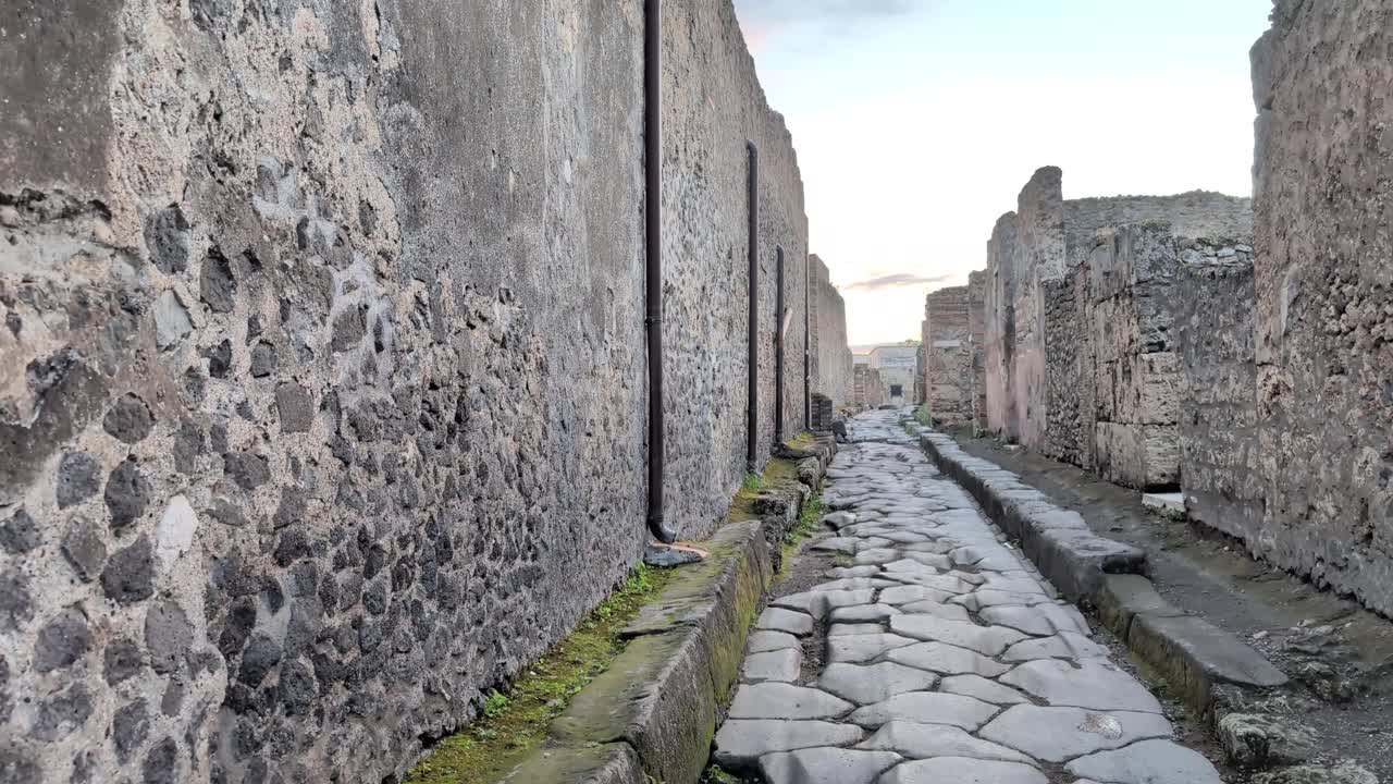 Slow pan right of a narrow stone street in Pompeii, Italy at golden hour, showing aged walls and cobblestones from the historic Roman city