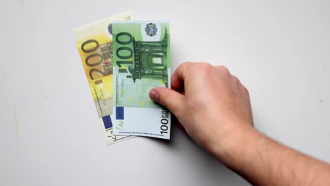 a person holding euros banknotes putting them on a clear background.