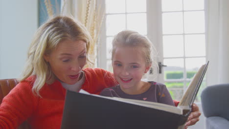Grandmother-And-Granddaughter-Looking-Through-Photo-Album-In-Lounge-At-Home-Together