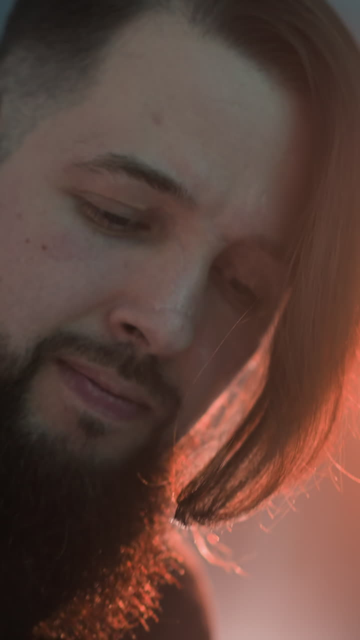 vista cercana de un hombre barbudo tocando una guitarra en una habitación iluminada con rojo. la luz suave y ambiental mejora su expresión enfocada mientras toca el instrumento