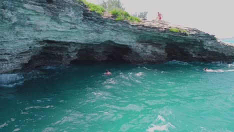 bermuda drone shot of divers swimming back towards caves under a cliff edge