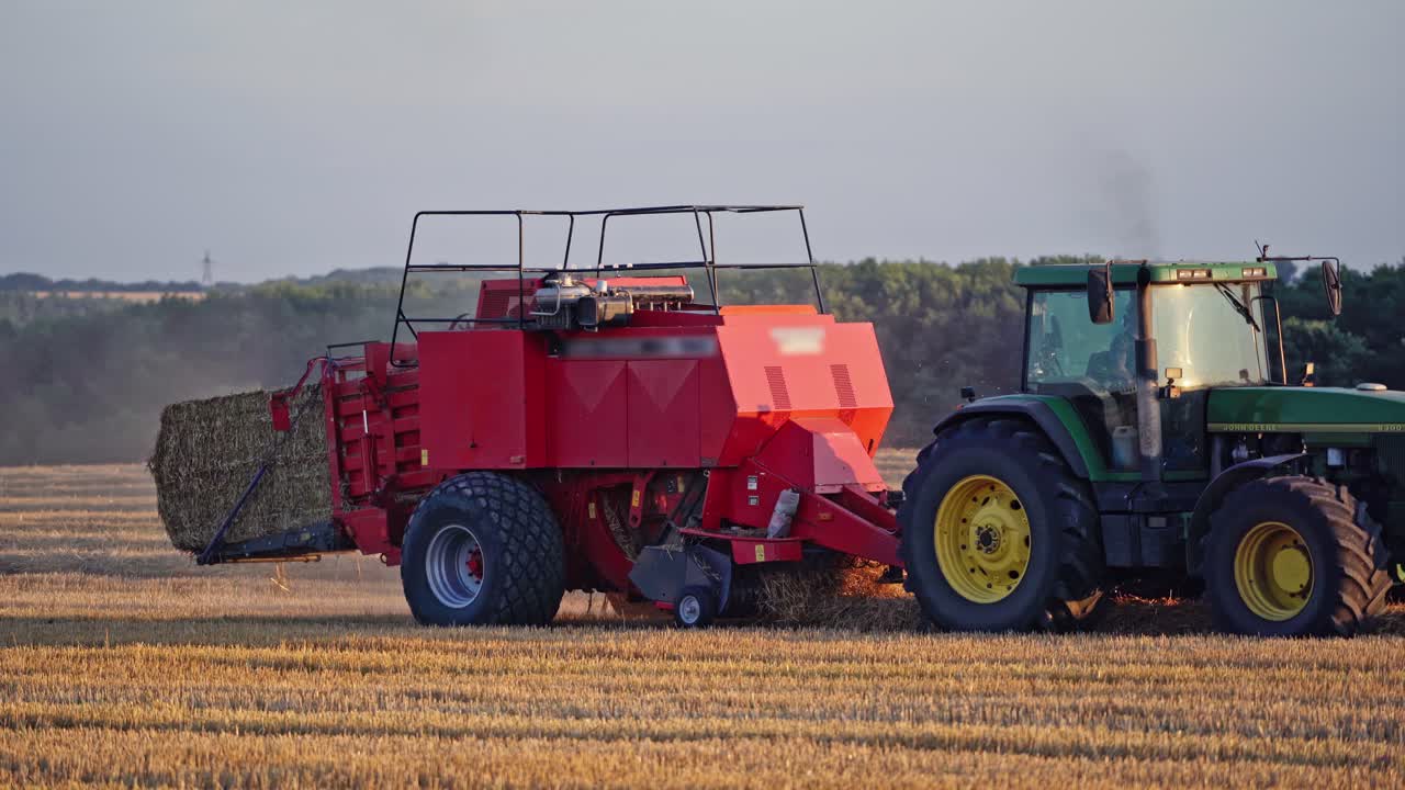 Modern tractor collects dry grass and pressing it into bale. Agricultural process of gathering hay on the golden field. Close-up.