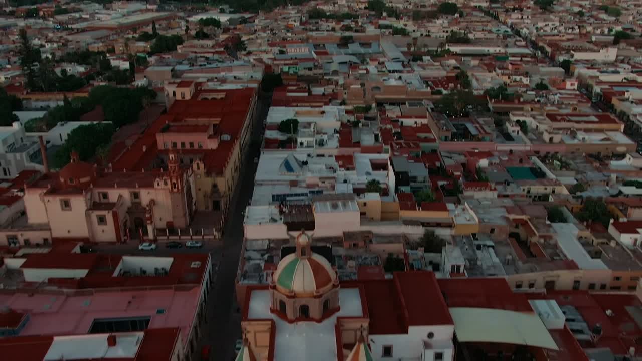 Ön planda ikiz kuleli kolonyal kilise. Querétaro, Meksika'da gün batımı gökyüzü altında Santiago de Querétaro şehir manzarasının geniş panoramik görünümü.
