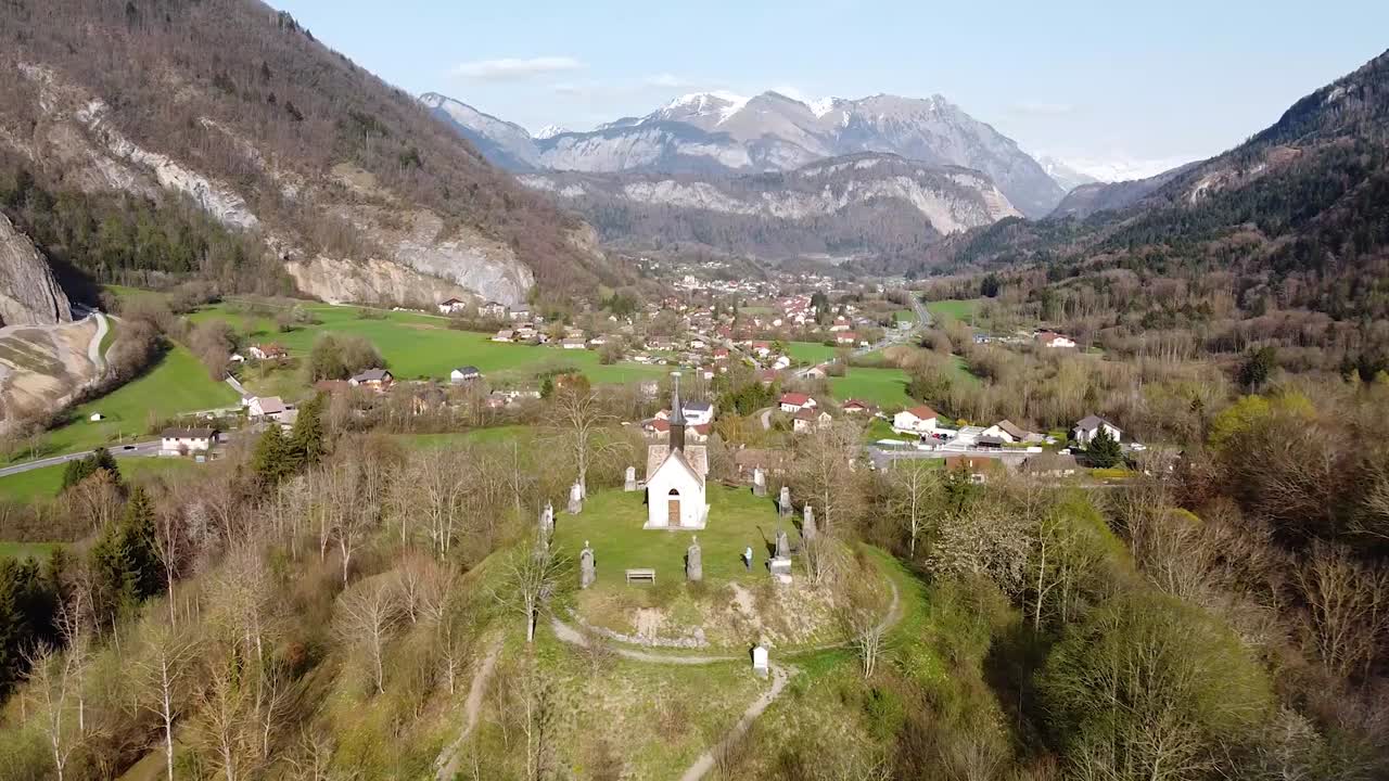toma de drones de una capilla en la cima de una colina frente a las montañas alpinas