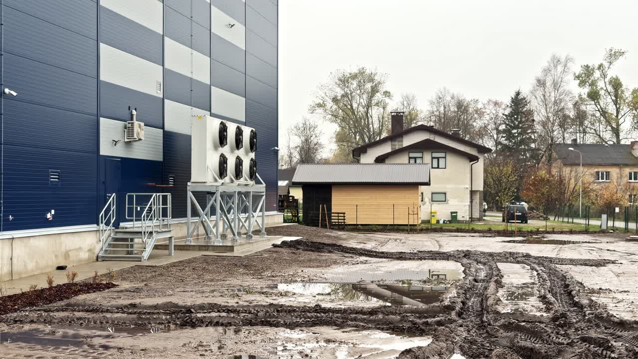 Industrial cooling fans and muddy tire marks site beside residential neighborhood in autumn