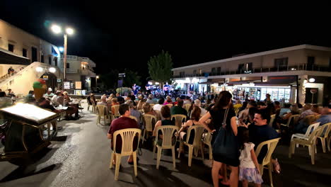 profile view of greek locals and tourists enjoying concert going on at agios nikolaos during nighttime.