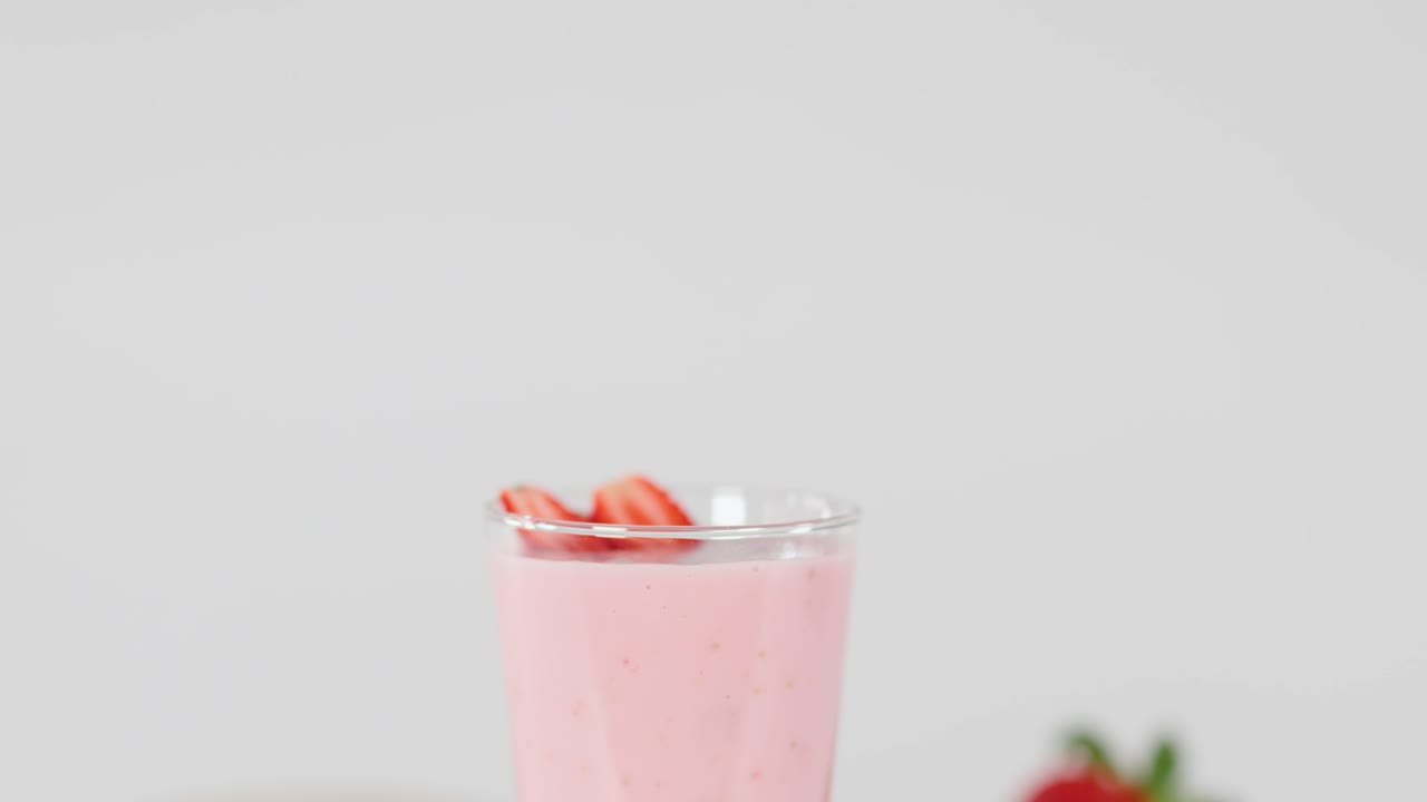 Red swirly straw inserted into creamy strawberry milkshake, bright lighting, colorful fresh fruit background