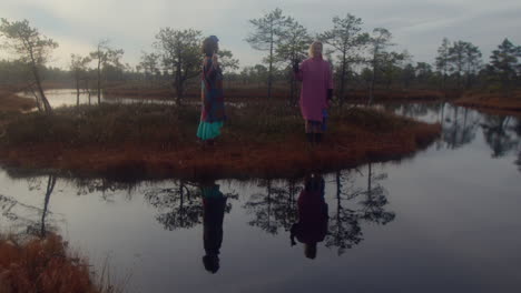 two women in artistic outfit standing in the swamp.