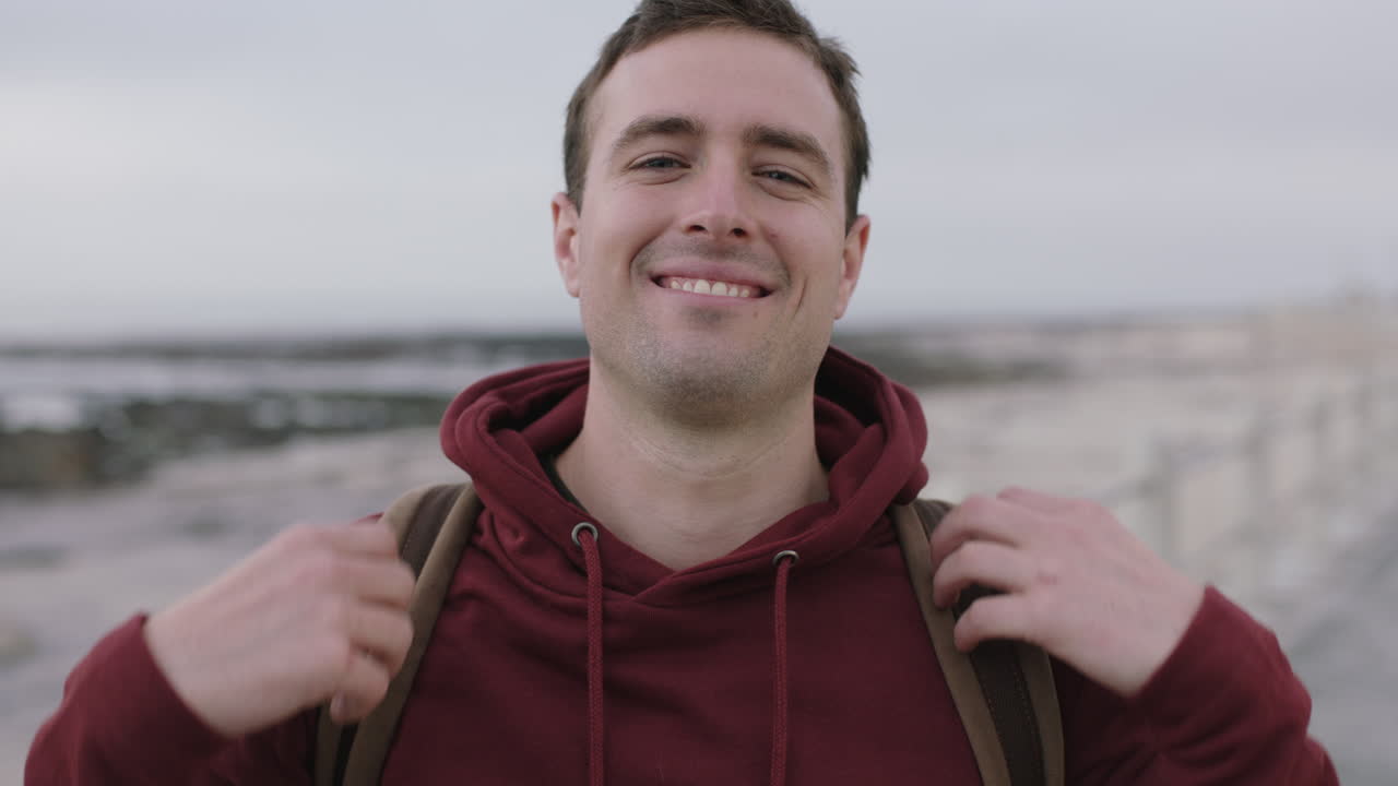 retrato de un joven guapo sonriendo con capucha en una playa costera fría