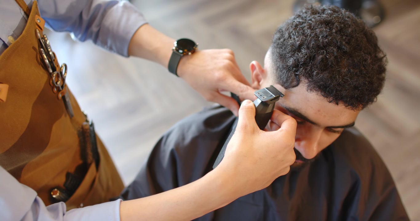 Barber placerer trimmer ved tindingen, trimmer hårgrænsen på mand i barberstol, forfiner fade.