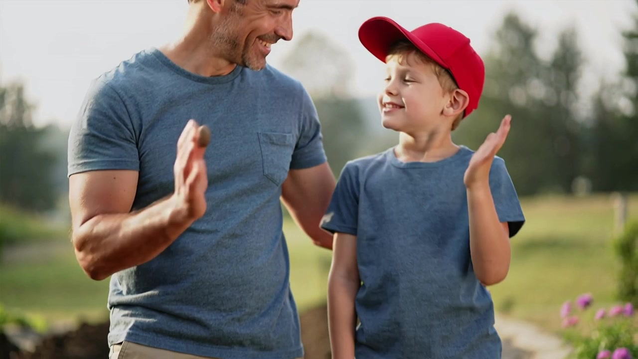 Inspecting palms after planting father and son exchanging high-five in garden, shovel and red cap