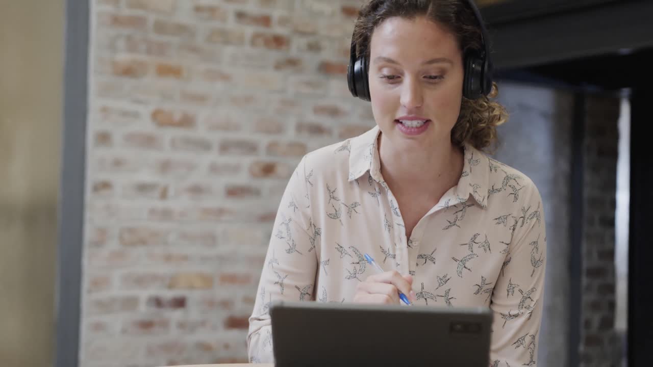 Kaukasisk afslappet forretningskvinde foretager videoopkald med en tablet i kontorloungen, slow motion