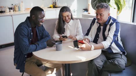 compañeros multiétnicos alegres navegando por teléfonos inteligentes en una cafetería