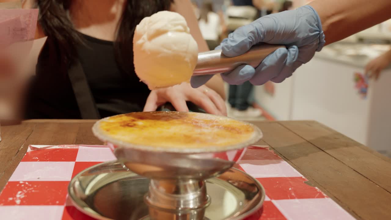Vendor putting a scoop of vanilla ice cream on top of Banana crème brûlée dessert