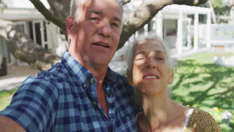 una feliz pareja de ancianos caucásicos tomando una selfie frente a la casa