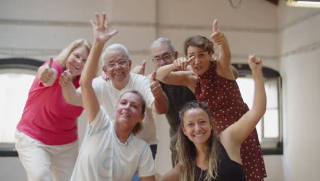 team of senior dancers standing in studio, showing thumbs up and sending kisses