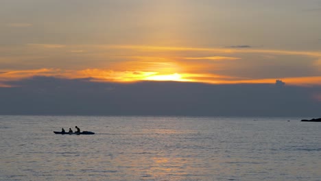 tourists in a rowboat at colorful orange sunset, silhouettes against the setting sun