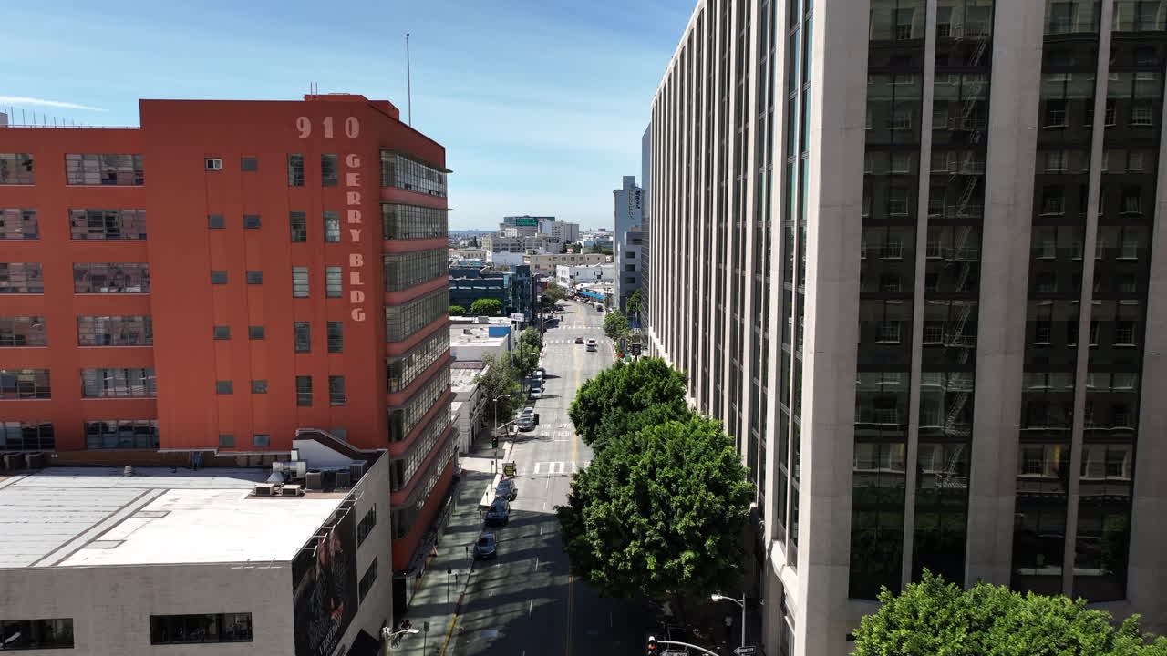 Amplia toma aérea del centro de Los Ángeles en el Distrito de la Moda, con edificios residenciales y comerciales de uso mixto y calles bulliciosas abajo. La escena muestra el entorno acelerado y la densa vida.