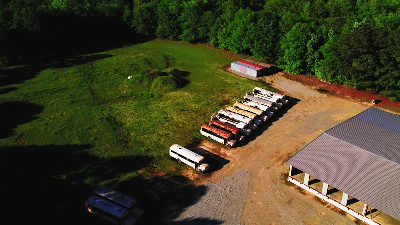 Abandoned School Buses Lined Up Beside Rural Building in Grassy Lot