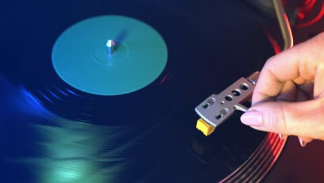 a young man puts a black vinyl record on the player with a close-up on a background of red and blue lights. the needle slides smoothly onto a rotating black vinyl record