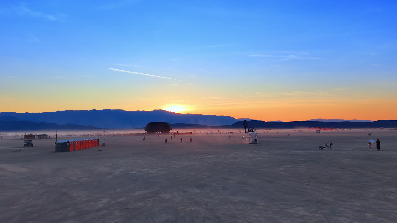 Nevada, USA, 25 August 2025: Aerial view of the desert horizon glowing at sunset during Burning Man festival with people and installations in the distance