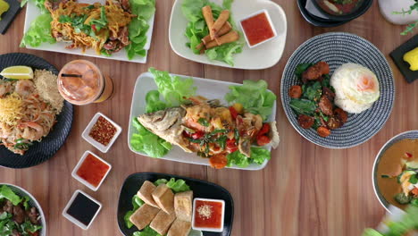 male hand placing pork pieces and condiments onto thai cuisine food flat lay