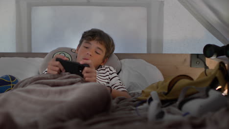 boy playing game on smartphone in bed