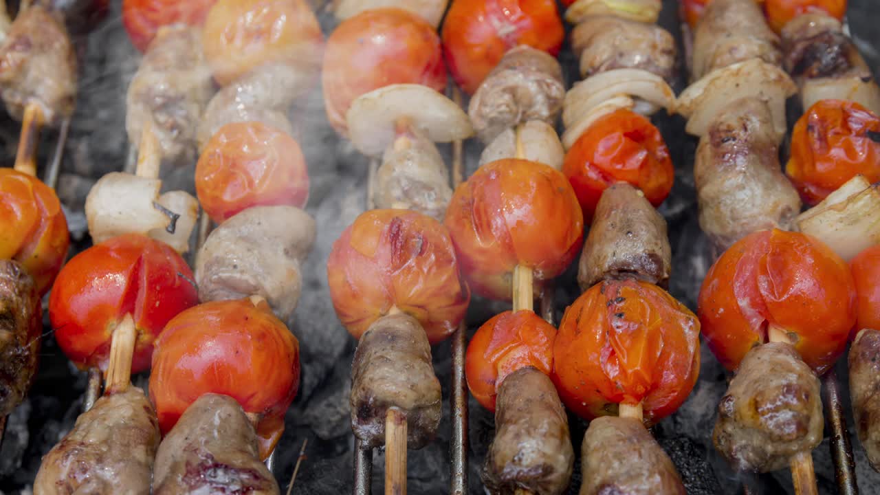 cinemagraph de humo emitido por cocinar corazones de pollo con tomate y cebolla en una parrilla de barbacoa caliente