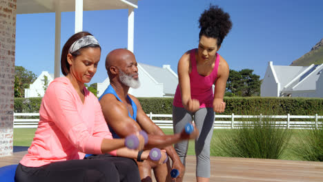 mixed-race personal trainer assisting senior black couple in exercising at backyard of their home 4k