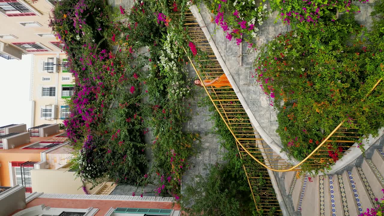 Vertical - Girl In Dress Climbing In Thang Rong Stairs Decorated With Colorful Flowers In Phu Quoc, Vietnam. drone shot