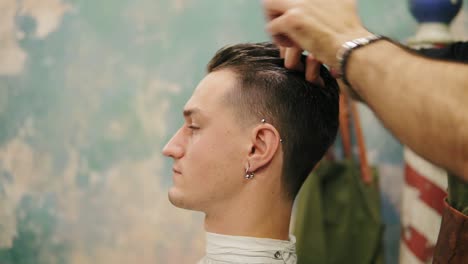 vista de cerca de las manos del peluquero aplicando cera en el cabello de un elegante cliente masculino en una toma de barbero. profesional