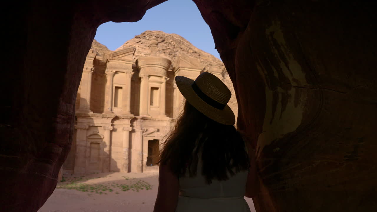 turista femenina dentro de la pequeña abertura de la cueva frente al monasterio de ad deir en petra, jordania