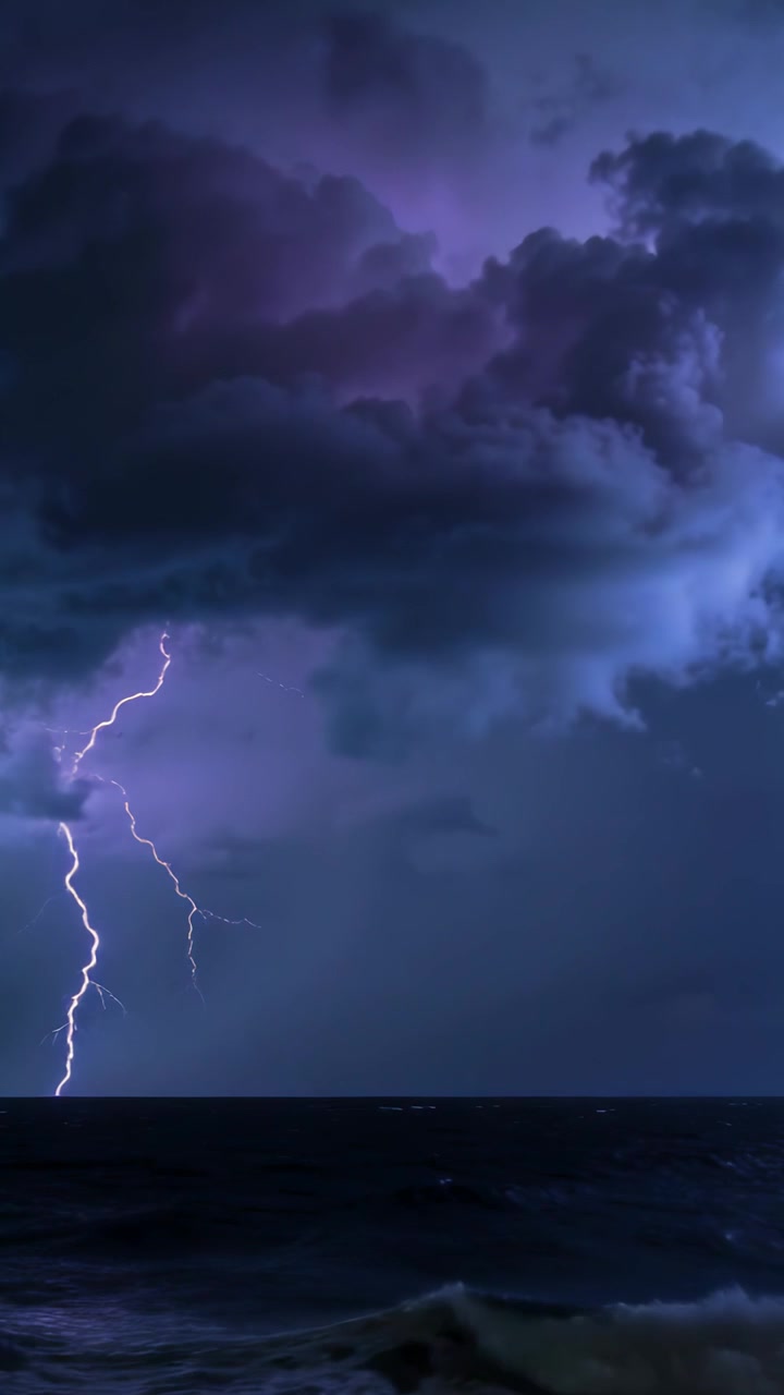 Vertical video: Charging storm clouds sparking jagged lightning over night ocean, sea water glowing