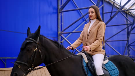 attractive dark-haired lady riding a beautiful black horse. woman practicing her hobby at riding hall. low angle view.